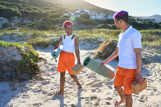 Gay couple with yoga mats walking on beach