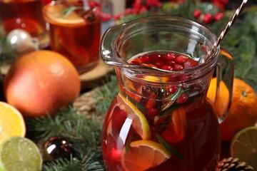 Tasty punch drink in glass jug, ingredients and Christmas decor on table, closeup