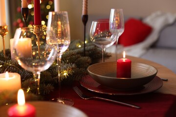 Beautiful dishware with burning candles, fir tree branches and Christmas lights on wooden table indoors, closeup