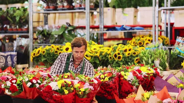 Attentive middle-aged salesman holding bouquet of flowers in large plants market. High quality 4k footage