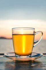 Cup of green tea front of at sunset light on wooden tabletop.