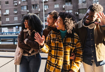 Happy multi ethnic friends greeting someone while walking in the city
