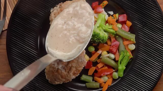A spoon pours bechamel over meatball jn a plate. High quality 4k footage