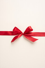 A vertical simple and elegant red ribbon bow tied on a soft neutral background, perfect for gift wrapping and special occasions