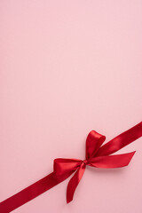 A vertical beautiful red satin ribbon tied in a bow adorning a pastel pink surface, perfect for special celebrations like Valentine's Day, weddings, or anniversaries