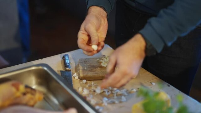 A man is cutting garlic on a wooden cutting board. The garlic is being chopped into small pieces
