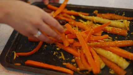A hand is touching a tray of carrots. The carrots are cut into thin strips and are sitting on a black tray