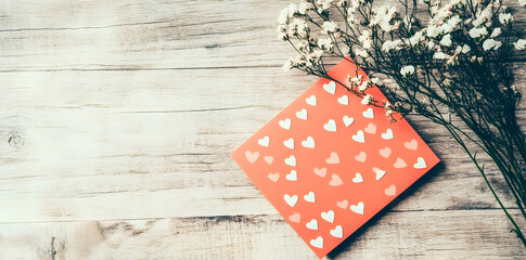 Obraz premium A red card adorned with white hearts beside delicate flowers on a wooden surface.
