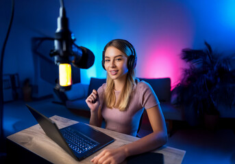 Young female podcaster, broadcasting a livestream to her viewers from home with microphone and laptop computer.