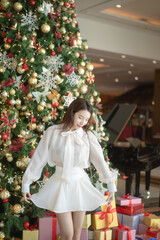 Woman in white dress in Christmas interior design, Christmas tree decorated by lights gifts lighting indoor.