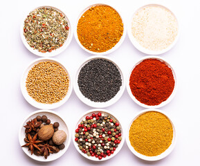 Bright set of aromatic organic spices and herbs such as smoked paprica, peppercorn, thyme, bay leaf, curry, dry garlic and others on white background top view.