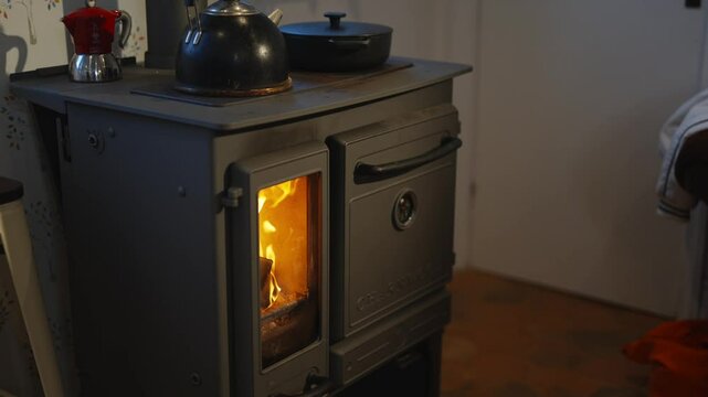 A stove with a pot on top of it and a teapot on the stove. The stove is lit and the pot is boiling