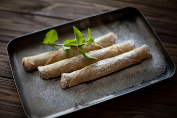 Rolled pancakes dusted with powdered sugar, garnished with fresh mint leaves, elegantly served on a vintage baking tray over a rustic wooden table.