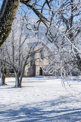 Vertical view of the church hidden behind snow covered trees in French Alps. Leoncel.