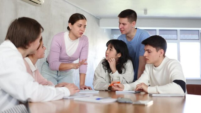 Smiling motivated young female team leader holding meeting with group of fellow students, explaining details of new study project