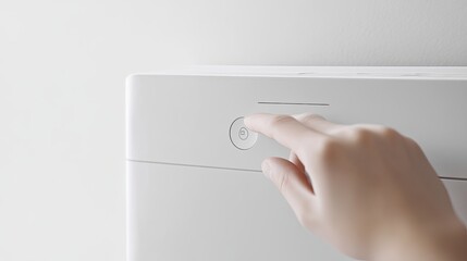 A hand presses a white power button on a white device.