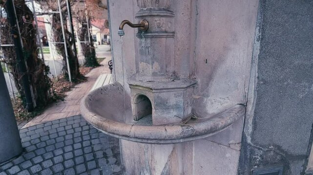 amera orbits from right to left around a faucet as it pours spa thermal water into a stone sink, focusing on the flowing water and surrounding details