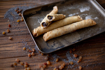 Golden-brown rolled pancakes with a rich poppy seed and raisin filling displayed on a vintage metal...