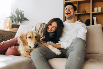 Happy couple laughing and relaxing on sofa with golden retriever