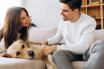 Happy couple petting their golden retriever dog on the sofa at home