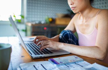 Stressed woman managing bills with laptop on kitchen desk