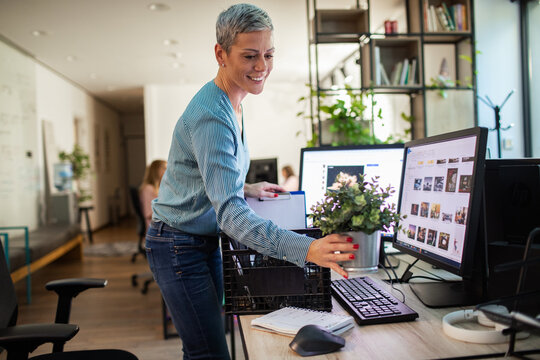 Smiling woman setting up workspace in office with potted plant