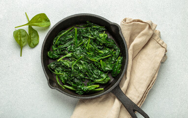 Freshly steamed spinach leaves are served in a cast iron pan, resting on a beige napkin, healthy...