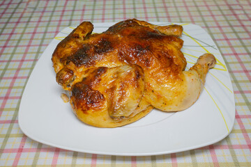 Whole roasted chicken on white plate with plaid tablecloth background