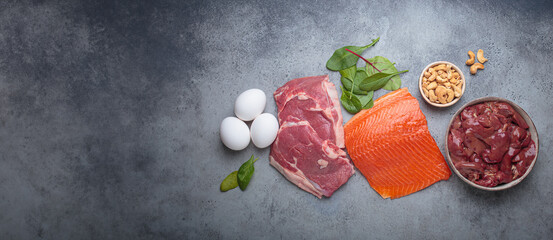 Fresh salmon fillet, raw beef, nutritious eggs, spinach, nuts cashews and liver arranged on a gray...