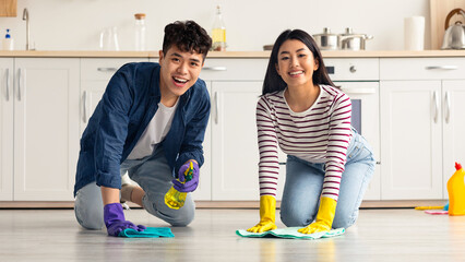 Young asian couple cleaning floor together at kitchen and smiling. Positive millennial korean man...