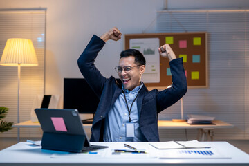 Excited businessman celebrating success while working on laptop in office at night