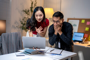 Asian business people looking shocked at tablet screen in office at night