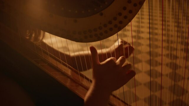Cropped shot of female harpist playing classical harp with soft golden light streaming from behind and illuminating her graceful hands