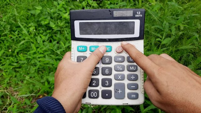 Person using an old calculator outdoors in a grassy area while pressing the clear button