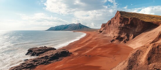 Aerial view of a stunning red sandy beach with cliffs and mountains under a vibrant sky by the sea. Perfect for travel and nature themes.