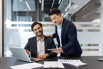 Two colleagues work together in a sleek office environment. They appear engaged and cooperative,...