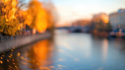 Serene river embankment adorned with golden autumn leaves basking in warm sunset light creating a tranquil blurred landscape scene.