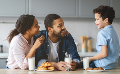 A joyful family shares a moment in their kitchen, with smiles and laughter. The parents engage their son as they enjoy cookies and milk, illustrating love and connection in their home.