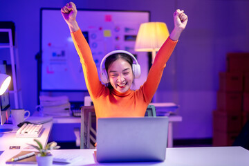 A woman in an orange shirt is celebrating with her hands in the air while sittin