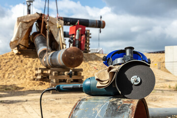 Ein Schleifgerät liegt auf einem Rohr auf einer Baustelle. Im Hintergrund wird ein Rohr mit einem Kran in Position gebracht