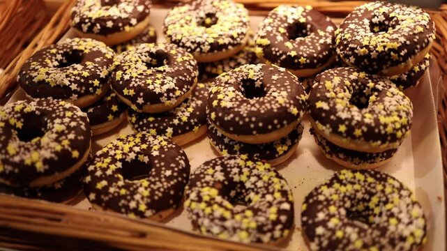 A tempting display of chocolate-glazed donuts decorated with yellow and white star sprinkles. The festive and delicious treat is arranged neatly in a wicker basket.
