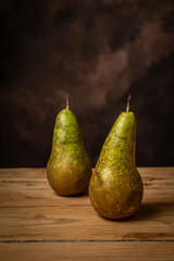 View of two pears on a wooden table, dark background, vertical with copy space