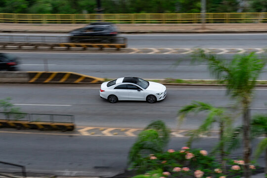 White Mercedes-Benz CLA with panoramic roof in motion, High angle panning shot of a luxury four-door coupe

