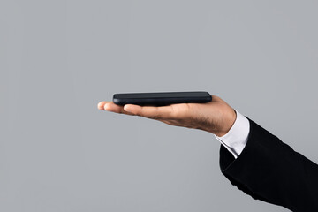 Unrecognizable businessman in formal attire holds a smartphone in his palm, closeup, cropped