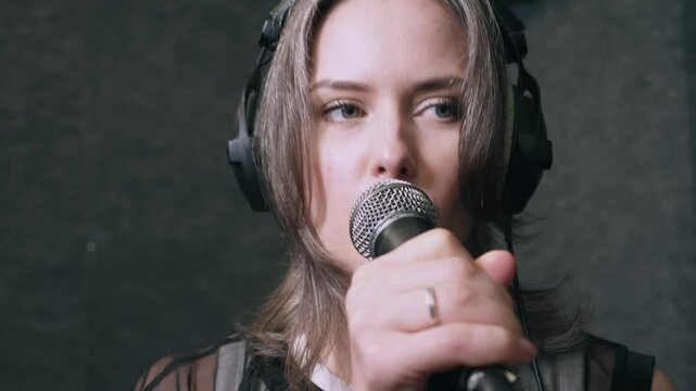 Modern female singer performing trap music in studio, wearing headphones and gripping microphone, intense expression and dynamic posture, professional recording setting.
