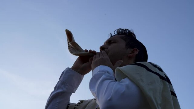 Young Jewish man playing the horn or shofar at dawn