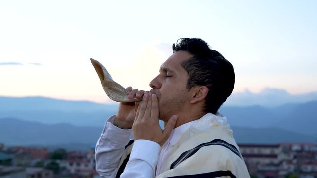 Jewish man uses tallit and blows shofar or horn to announce the feast of trumpets and the new year