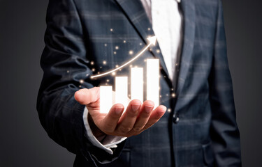 Businessman holding illuminated bar graph with sparkles symbolizing financial success and upward economic growth