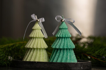 Two scented Christmas candles in the shape of Christmas trees with bows and small bells on a black plaster stand