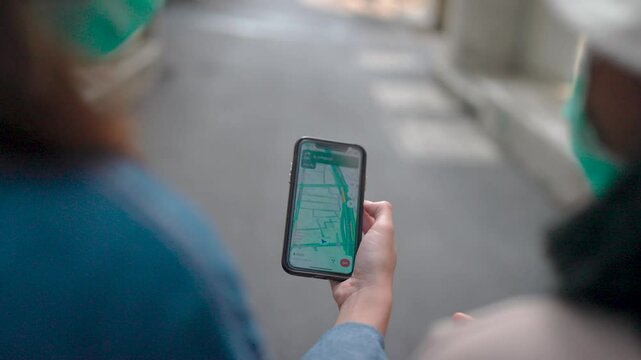 Navigating the City.A close-up shot of a person's hand holding a smartphone displaying a map app, with another person in the background wearing a mask.